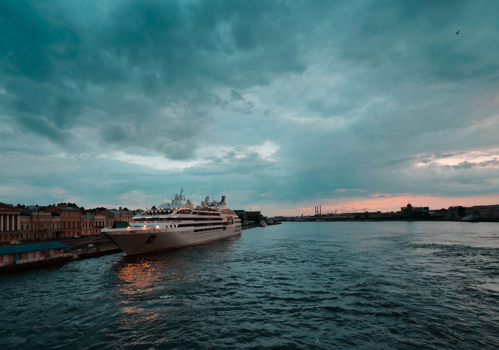 Small cruise ship sailing past a historic waterfront under a dramatic evening sky