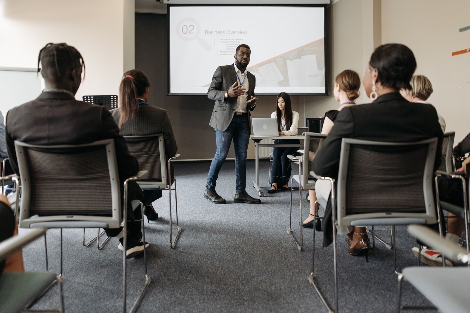 Presenter speaking to a seated audience in front of a screen, sharing a travel agency marketing strategy