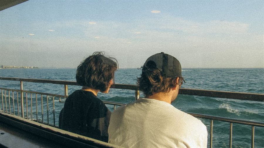 Two travelers at a ship rail looking out to sea